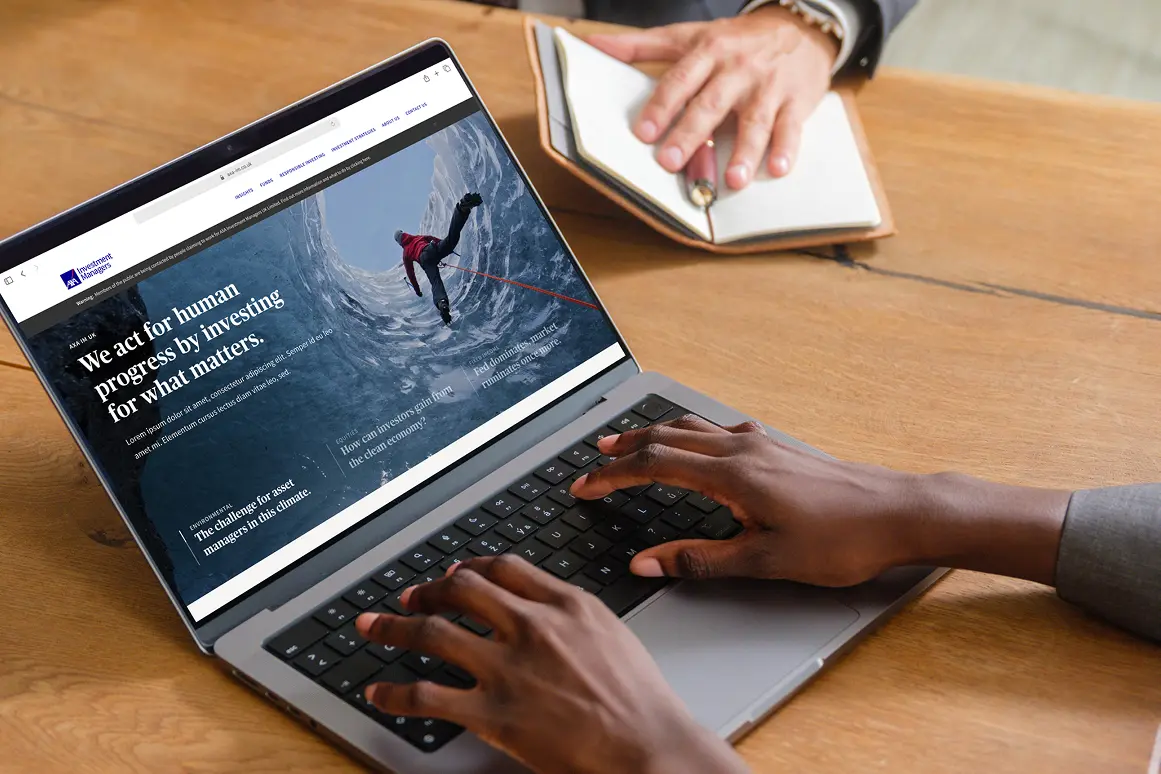 Person typing on a laptop showing the AXA IM homepage, 'We act for human progress by investing for what matters'
