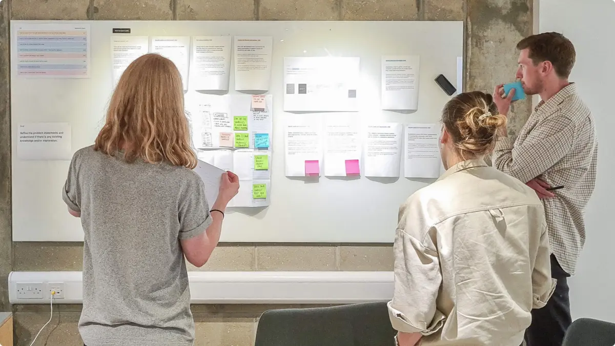 Three people reviewing research notes and sticky notes on a whiteboard