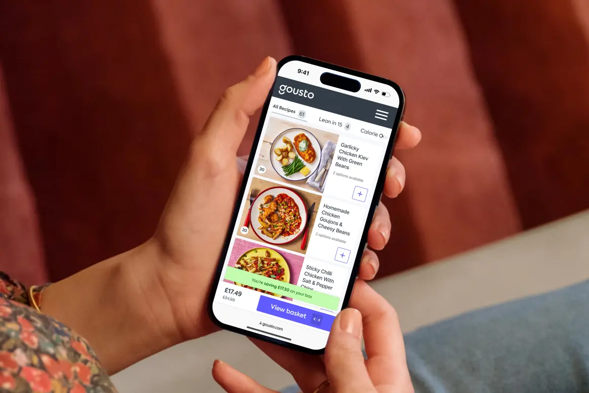 Hands holding a phone showing the Gousto recipe menu with a 'View basket' button